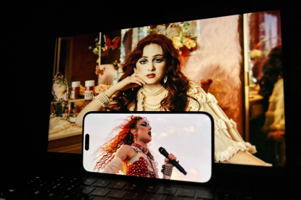 Artist Chappell Roan sitting backstage behind smart phone showing her performing