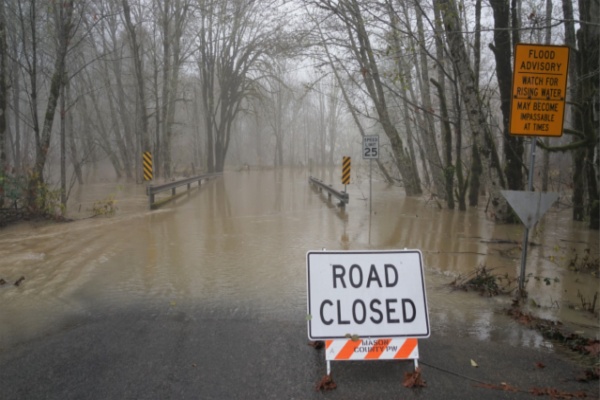 Flooded road through trees behind Road Closed sign