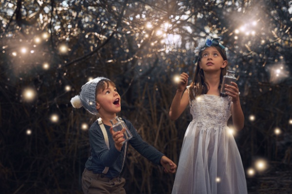 Young boy and girl look up at night sky trying to catch fireflies around them