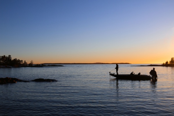 two men lake fishing on a boat at sunset