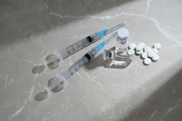 Two medical syringes lie on table next to liquid medicine andpills