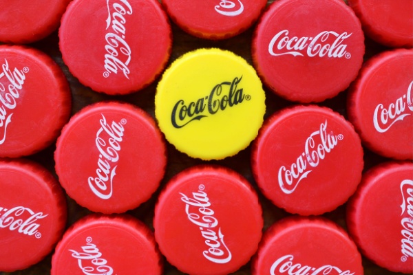 Overhead view of a bunch of red bottle caps reading "Coca-Cola," one is yellow