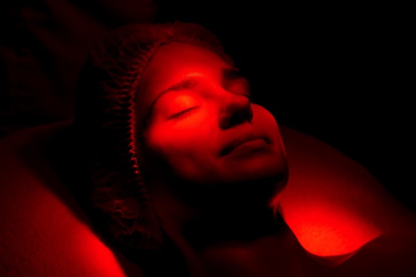 Woman on facialist table smiles with eyes closed under red light therapy glow