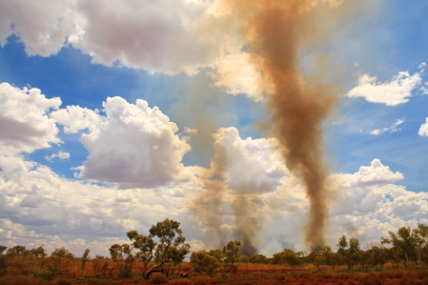 Plumes from a smoke fire whirl go skyward against blue sky and white clouds