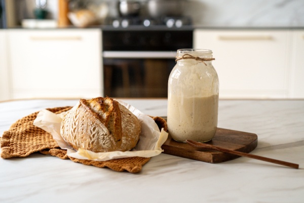 Sourdough bread loaf next to jar of starter on kitchen counter