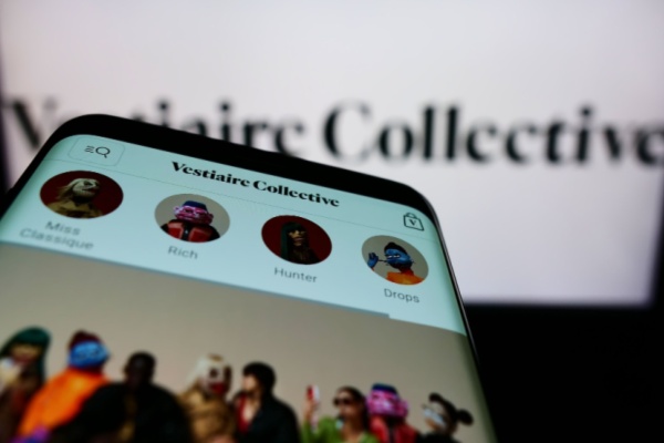 Smart phone with Vestiaire Collective shopping site open in front of computer screen with the site open