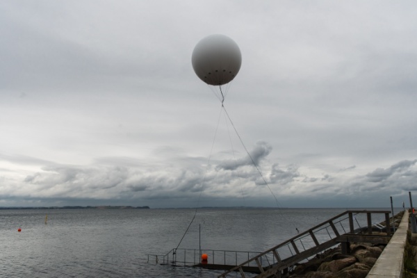 White weather balloon floats above the sea on a cloudy day