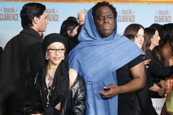 A photo of rapper Doja Cat and Jeymes Samuel on the red carpet. Doja is wearing glasses and all black, while Jeymes is wearing blue.