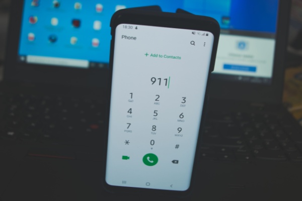 smartphone propped up in front of computer screen showing 911